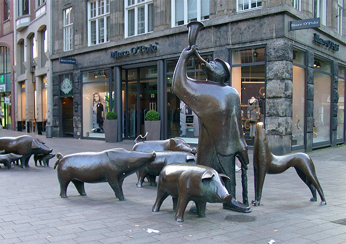 Side view of the monument "Shepherd with pigs". It shows the shepherd with his dog and the pigs. In his hands he carries a horn and a stick.